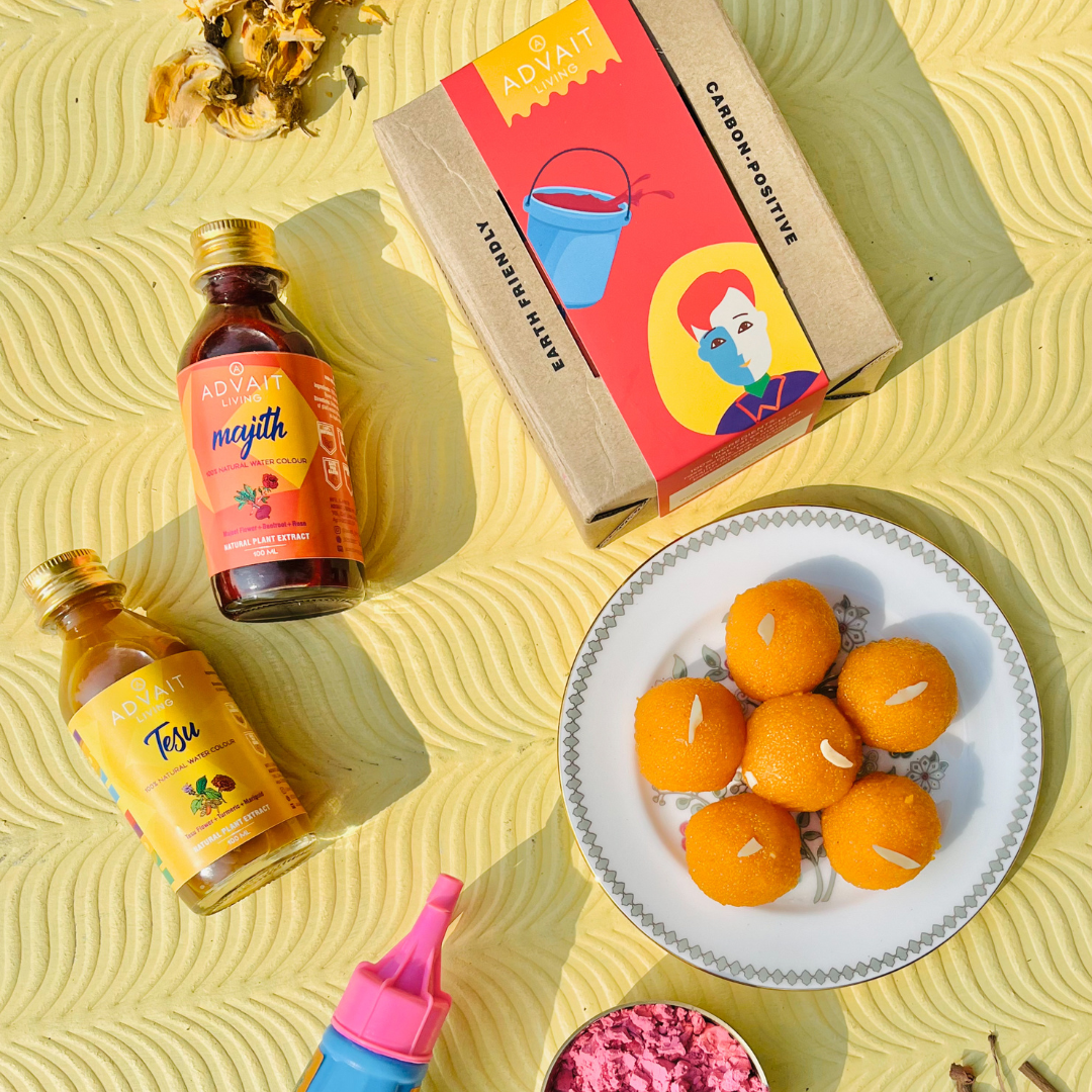 Two bottles of water colours on table with box and a plate of laddoos