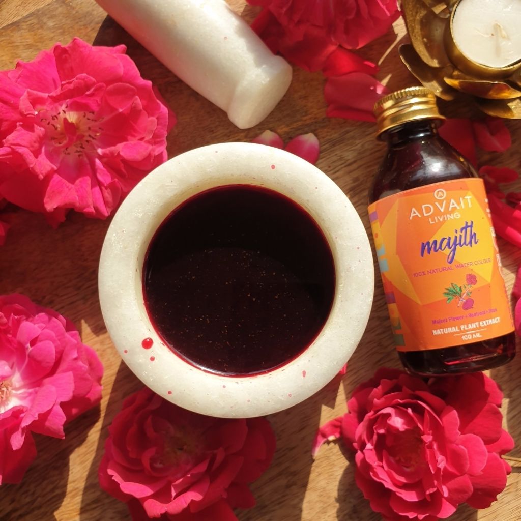 A bottle and a bowl containing Majith water colour on a table with rose petals.