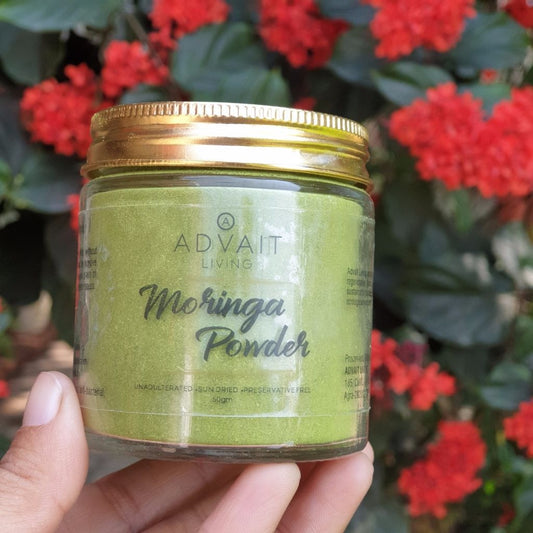 A hand holding a 50 gm glass bottle of Advait Living Moringa Powder.